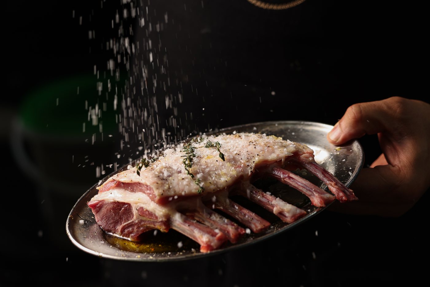 A rack of lamb seasoned by hand before the grill